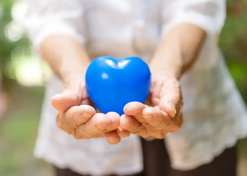Hände einer älteren Frau hält ein blaues Herz